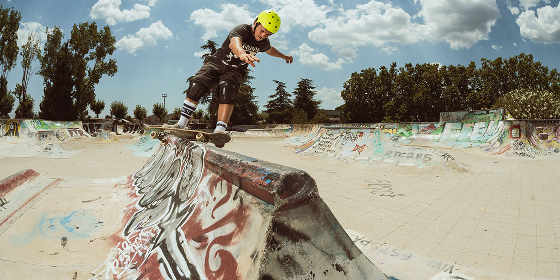 Skateboarder wearing a yellow Ancore skate helmet at a graffiti-covered skatepark